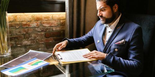 A businessman in a suit reviewing financial documents at a desk in an office setting.